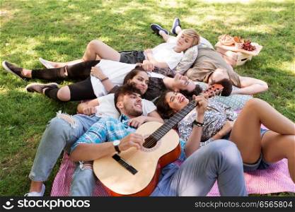 friendship, leisure and summer concept - group of happy smiling friends with guitar chilling on picnic blanket. friends with guitar chilling on picnic blanket