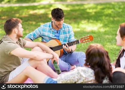 friendship, leisure and summer concept - group of happy smiling friends with guitar and non alcoholic beer chilling on picnic blanket at summer park. friends playing guitar at picnic in summer park