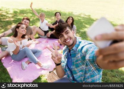 friendship, leisure and technology concept - group of happy smiling friends taking selfie by smartphone chilling on picnic blanket at summer park. friends taking selfie by smartphone at picnic. friends taking selfie by smartphone at picnic