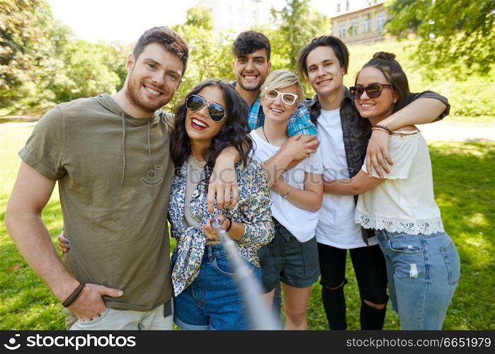 friendship, leisure and technology concept - group of happy smiling friends taking picture by selfie stick at summer park. friends taking picture by selfie stick at summer