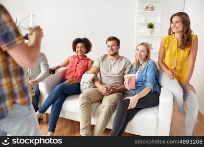 friendship, leisure, communication and entertainment concept - happy friends with popcorn and drinks talking at home