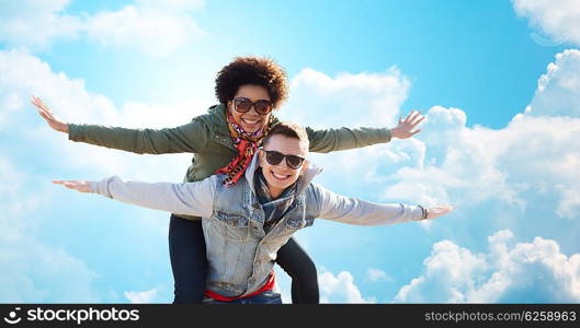 friendship, leisure, freedom and people concept - happy international teenage couple in shades having fun over blue sky and clouds background