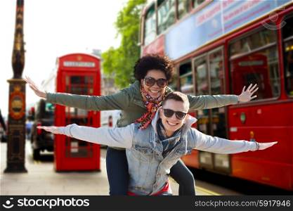friendship, leisure, international, freedom and people concept - happy teenage couple in shades having fun over london city bus on street background