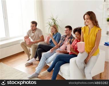 friendship, leisure, junk food, people and entertainment concept - happy friends eating popcorn and watching tv at home