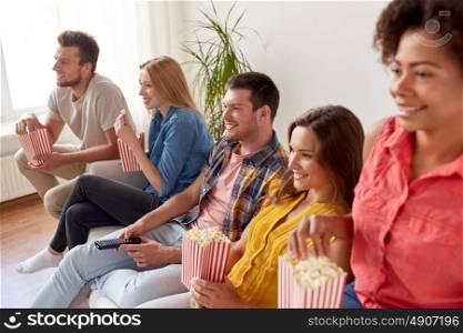 friendship, leisure, junk food, people and entertainment concept - happy friends eating popcorn and watching tv at home. happy friends with popcorn watching tv at home