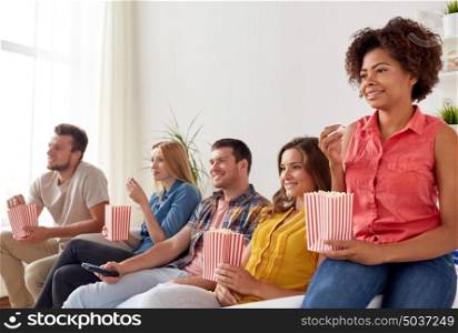 friendship, leisure, junk food, people and entertainment concept - happy friends eating popcorn and watching tv at home. happy friends with popcorn watching tv at home