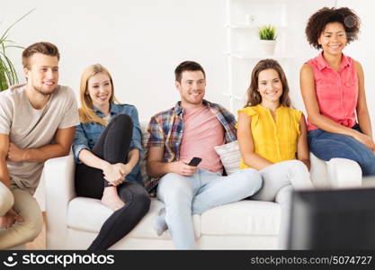 friendship, leisure, junk food, people and entertainment concept - happy friends with remote watching tv at home. happy friends with remote watching tv at home