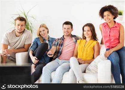 friendship, leisure, junk food, people and entertainment concept - happy friends with remote watching tv at home. happy friends with remote watching tv at home
