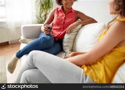 friendship, leisure, people and communication concept - close up of happy women with drinks sitting on sofa and talking at home