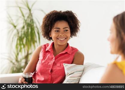 friendship, leisure, people and communication concept - happy woman with drink sitting on sofa and talking to her friend at home