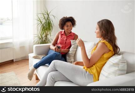 friendship, leisure, people and communication concept - happy women with drink sitting on sofa and talking gat home
