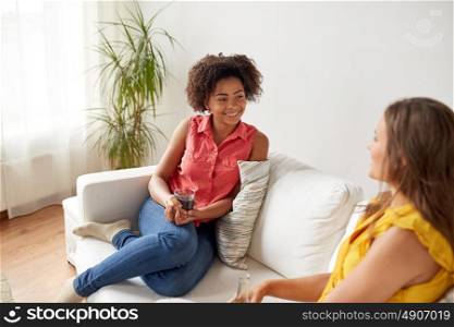 friendship, leisure, people and communication concept - happy women with drink sitting on sofa and talking gat home. happy women with drink talking gat home