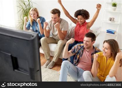 friendship, leisure, people and entertainment concept - happy friends with remote control and drinks watching tv at home