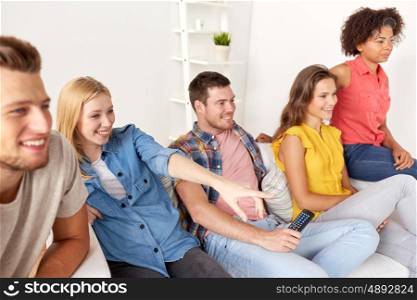 friendship, leisure, people and entertainment concept - happy friends with remote watching tv at home