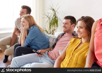 friendship, leisure, people and entertainment concept - happy friends with remote watching tv at home