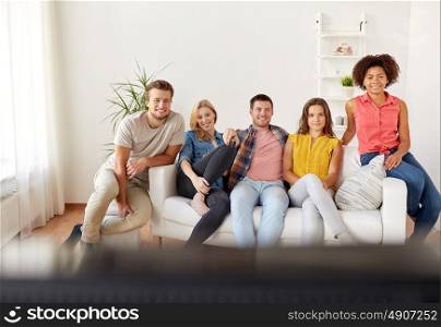 friendship, leisure, people and entertainment concept - happy friends with remote watching tv at home. happy friends with remote watching tv at home