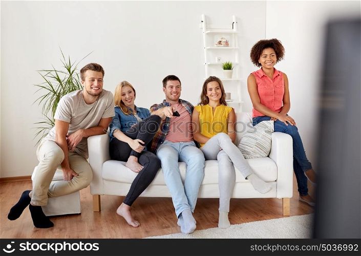friendship, leisure, people and entertainment concept - happy friends with remote watching tv at home. happy friends with remote watching tv at home