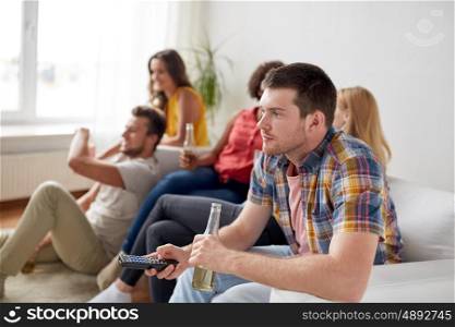 friendship, leisure, people and entertainment concept - happy man with remote control watching tv and drinking beer or cider with friends at home