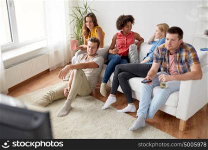 friendship, leisure, people and entertainment concept - happy man with remote control watching tv and drinking beer or cider with friends at home. friends with popcorn and beer watching tv at home