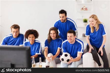 friendship, leisure, sport and entertainment concept - happy friends or football fans with ball watching soccer on tv at home. friends or football fans watching soccer at home
