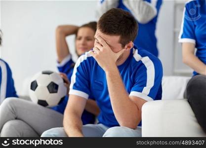 friendship, leisure, sport and entertainment concept - unhappy man with friends or football fans at home