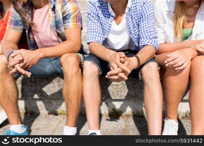 friendship, leisure, summer and people concept - close up of friends legs sitting on city square