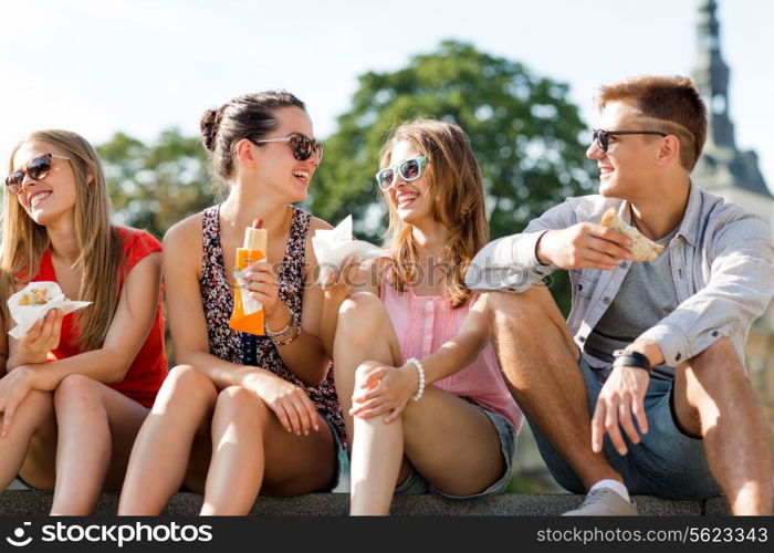 friendship, leisure, summer and people concept - group of smiling friends in sunglasses sitting with food on city square