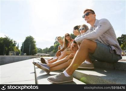 friendship, leisure, summer and people concept - group of smiling friends in sunglasses sitting on city street