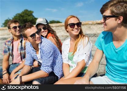 friendship, leisure, summer and people concept - group of smiling friends in sunglasses sitting on city street