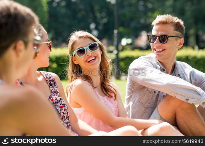 friendship, leisure, summer and people concept - group of smiling friends outdoors sitting on grass in park