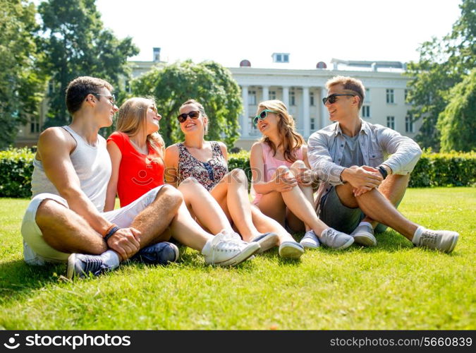 friendship, leisure, summer and people concept - group of smiling friends outdoors sitting and talking on grass on grass in park