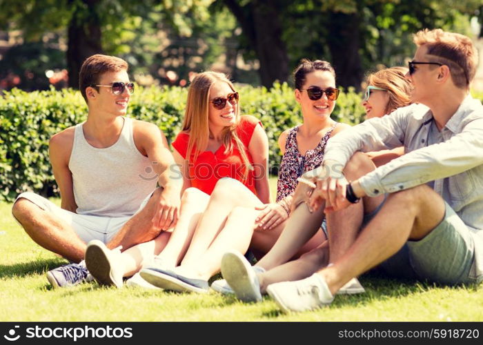 friendship, leisure, summer and people concept - group of smiling friends outdoors sitting on grass in park