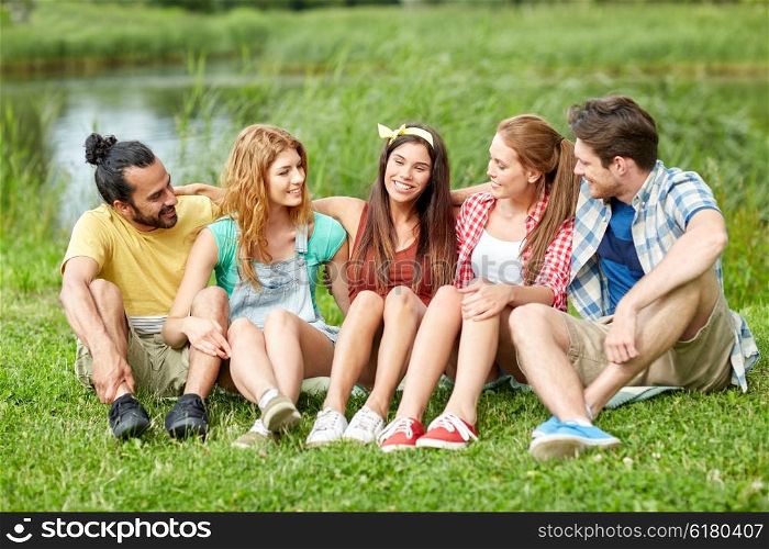 friendship, leisure, summer and people concept - group of smiling friends sitting on grass and talking outdoors