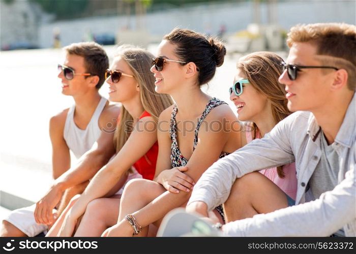 friendship, leisure, summer and people concept - group of smiling friends sitting on city square