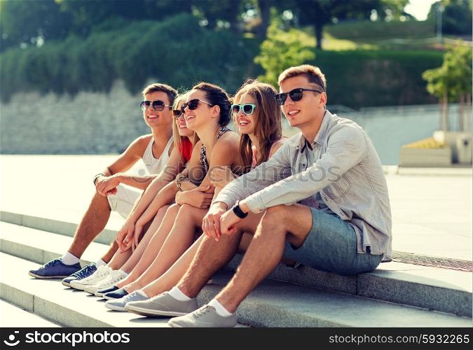 friendship, leisure, summer and people concept - group of smiling friends sitting on city square