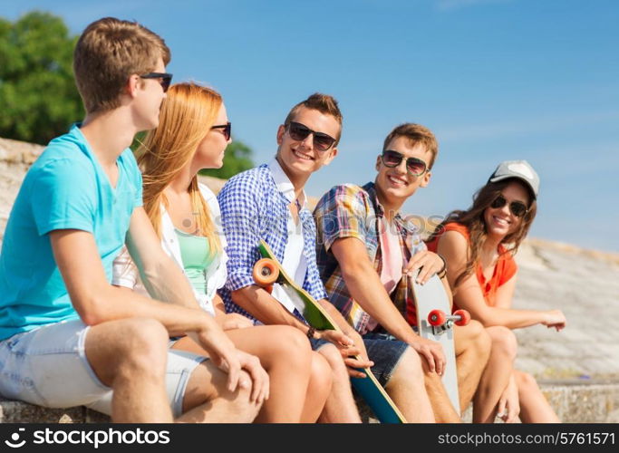 friendship, leisure, summer and people concept - group of smiling friends with skateboards sitting on city street