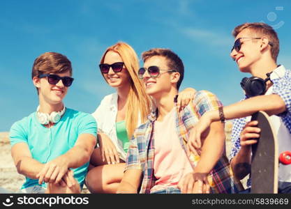 friendship, leisure, summer and people concept - group of smiling friends with skateboard sitting on city street