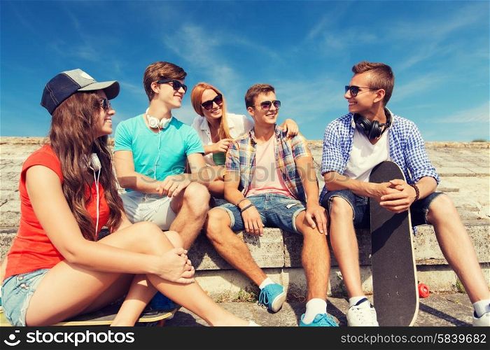 friendship, leisure, summer and people concept - group of smiling friends with skateboards sitting on city street