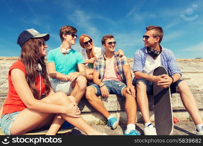 friendship, leisure, summer and people concept - group of smiling friends with skateboards sitting on city street