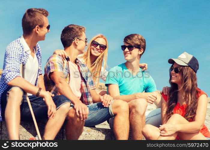 friendship, leisure, summer and people concept - group of smiling friends with skateboard sitting on city street