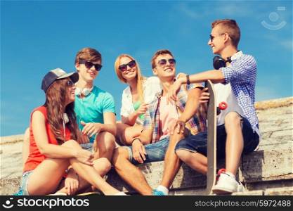 friendship, leisure, summer and people concept - group of smiling friends with skateboard sitting on city street