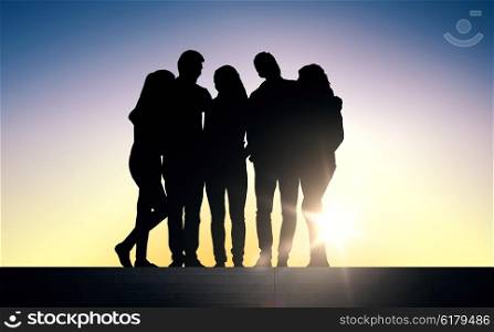 friendship, leisure, summer and people concept - silhouettes of friends sitting on stairs over sun light background