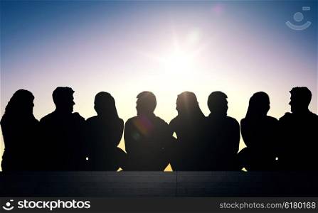 friendship, leisure, summer and people concept - silhouettes of friends sitting on stairs over sun light background