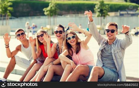 friendship, leisure, summer, gesture and people concept - group of laughing friends sitting on city square