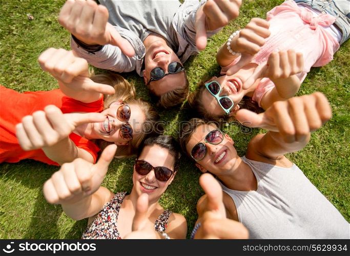 friendship, leisure, summer, gesture and people concept - group of smiling friends lying on grass in circle and showing thumbs up outdoors