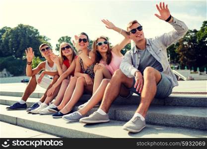 friendship, leisure, summer, gesture and people concept - group of smiling friends sitting on city street and waving hands
