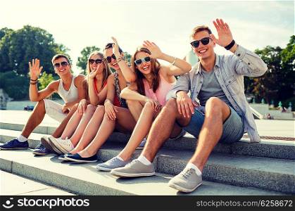 friendship, leisure, summer, gesture and people concept - group of smiling friends sitting on city street and waving hands