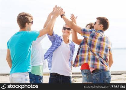 friendship, leisure, summer, gesture and people concept - group of smiling friends making high five outdoors