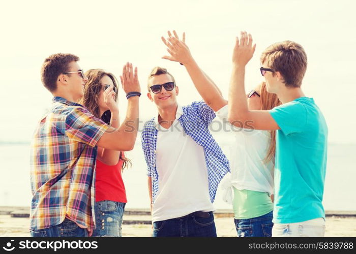 friendship, leisure, summer, gesture and people concept - group of smiling friends making high five outdoors