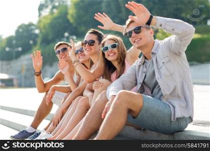 friendship, leisure, summer, gesture and people concept - group of smiling friends sitting on city square